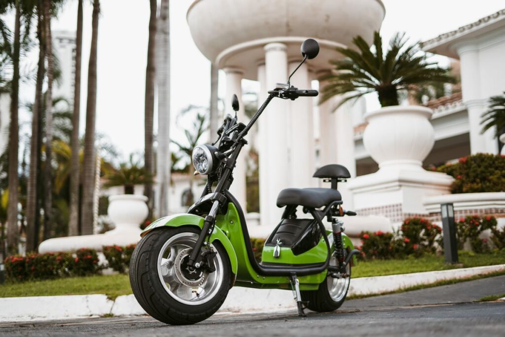 Moto eléctrica verde estacionada en una calle con palmeras