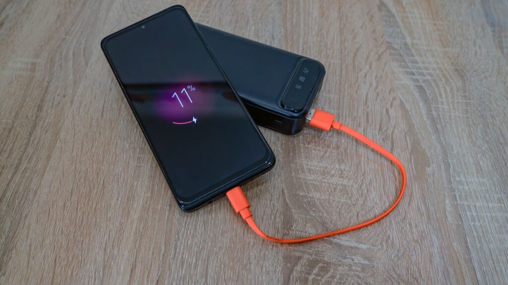 Phones With 8000mAh to 10001mAh Batteries for Multi-Day Use Smartphone charging from a power bank on a wooden table