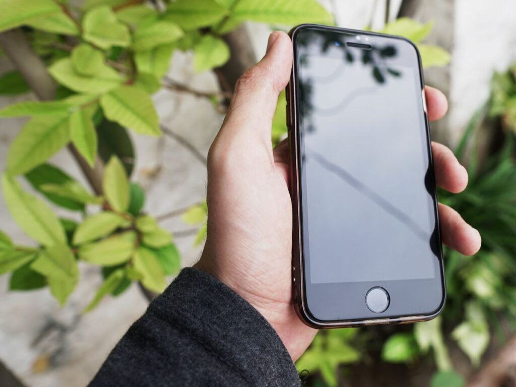 Hand holding a modern smartphone next to green plants